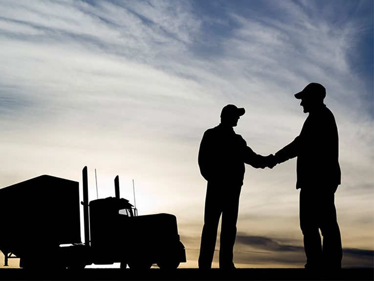 image of two drivers shaking hands, a truck in the background, all of it silhouetted