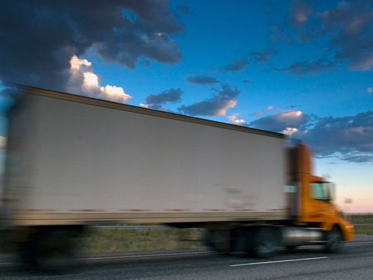 image of orange and white semi driving on road, blurred to show motion