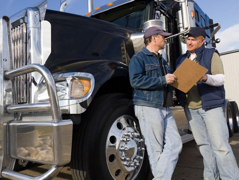 image of two truck drivers leaning against black semi looking at clipboard