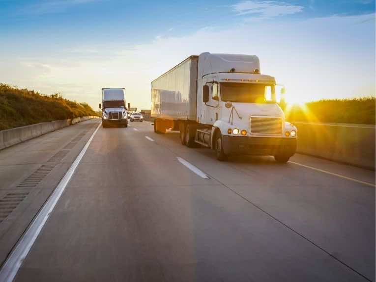 image of two white semi trucks driving away from the sunset