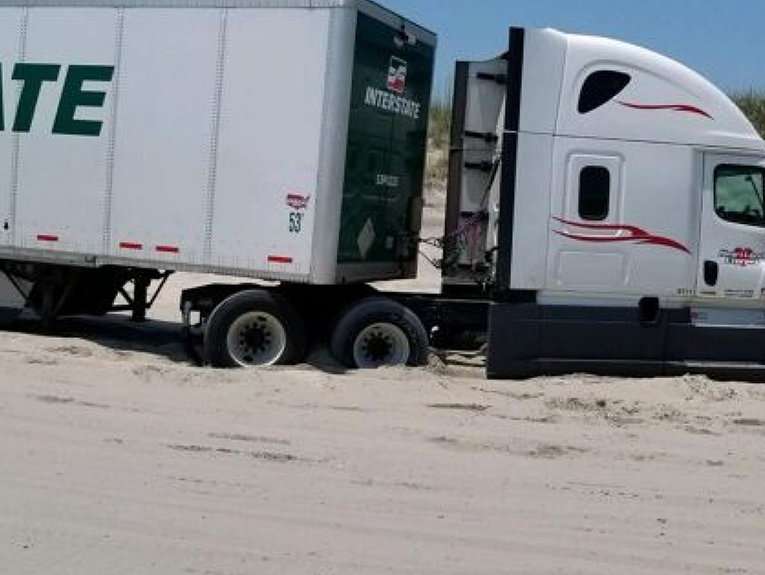 Large white truck stuck in sand on beach