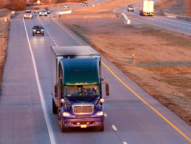 image of semi driving on road, cars following behind