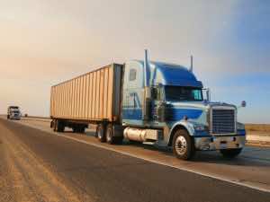 white and blue truck driving on road, another truck following behind