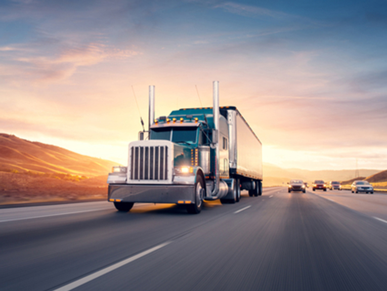 image of blue and white semi driving on busy highway during sunset, blurred to show motion