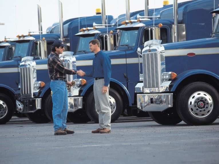 image of truck drivers shaking hands, a row of blue semi trucks parked behind