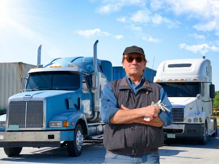 image of truck driver, arms crossed, standing in front of blue and white semi trucks