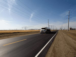 white tanker truck driving on road next to fields
