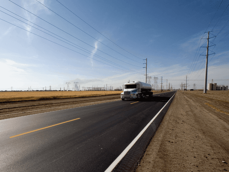 Image of white tanker truck driving on road next to fields