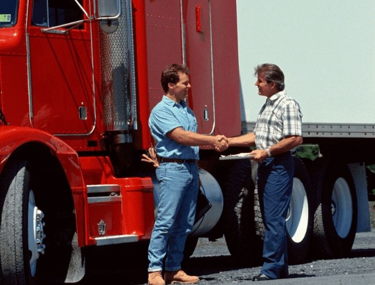two men shaking hands in front of a red semi truck