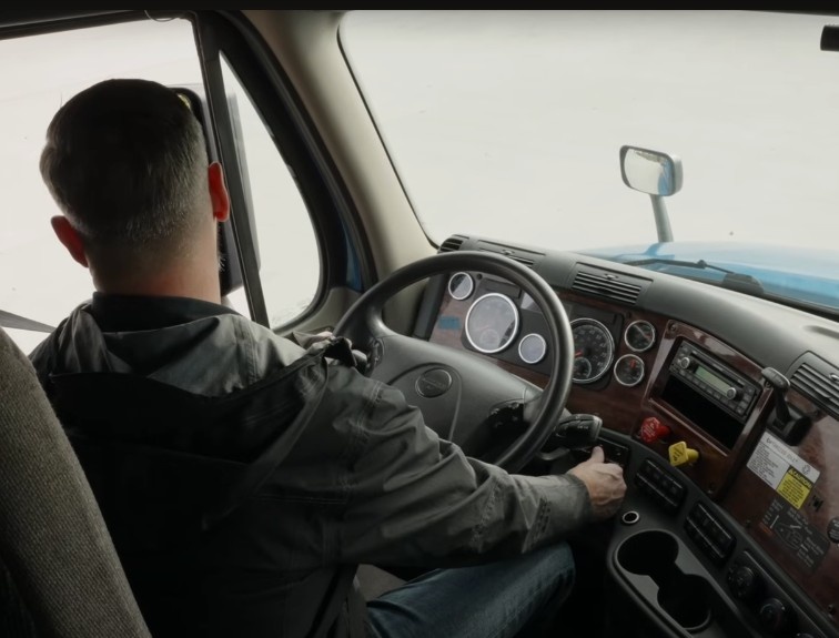 Truck driver sitting behind the wheel, holding gear shift
